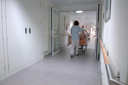 Pflegepersonal schiebt Patient im Rollstuhl durch den Flur eines medizinischen Instituts