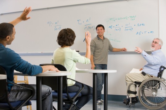 Lehrer im Rollstuhl und Schüler vor einer Tafel