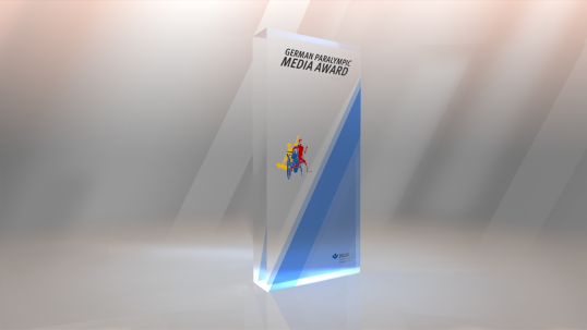 Das Bild zeigt den Preis: Eine rechteckige Glassäule mit eingeätzem Text, farbigem Logo aus Menschen mit Behinderung beim Sport