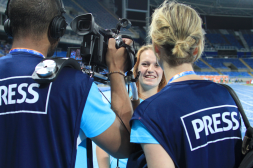 Ein Kameramann links und eine Redakteurin sind von hinten zu sehen, wie sie für die PZ eine strahlende Sportlerin interviewen.
