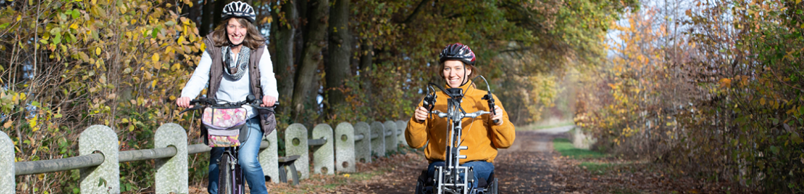 Bild zeigt Sabrina Busch im Handbike neben Ihrer Mutter aufde Rad durch einen Wald fahren.