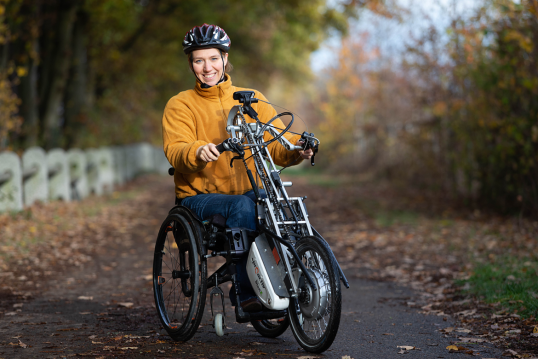 Sabrina Busch steht mit ihrem Handbike auf einem Waldweg.