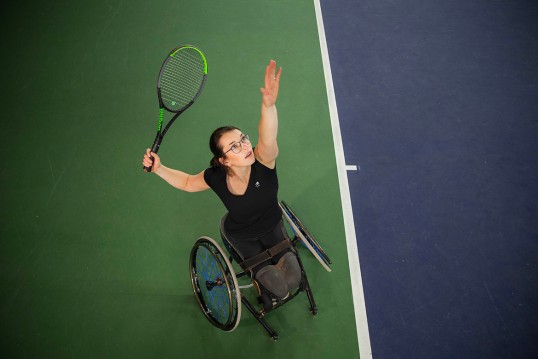 Bild zeigt Britta Wend von oben, wie Sie im Rollstuhl sitzend den Ball hochwirft und mit dem Schläger ausholt.