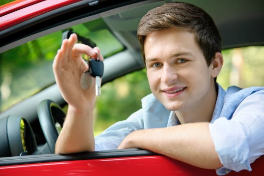 ein junger Erwachsener schaut aus einem Auto und hält einen Autoschlüssel in der Hand