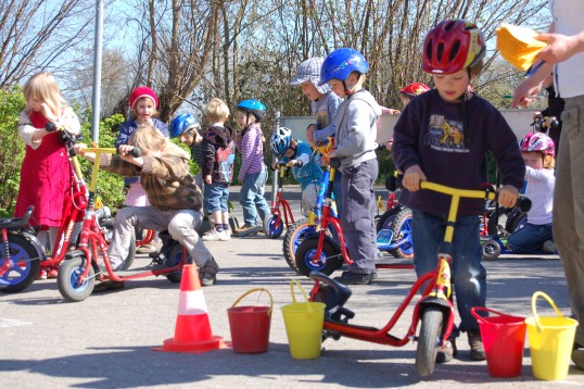 Kindergartenkinder mit Rollern und Fahrrädern im Parcours