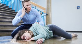 Foto: Ein junger Mann kniet neben einer ohnmächtigen Frau und macht einen Notruf mit seinem Handy 