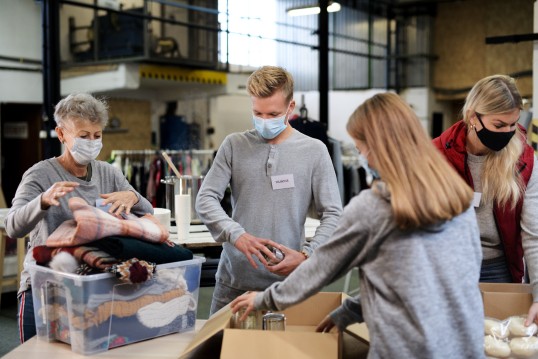 Vier Personen sortieren Spenden und tragen dabei eine Mund-Nase-Bedeckung