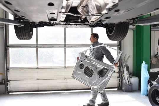 Mann trägt verzinkte Autotür durch Werkstatthalle