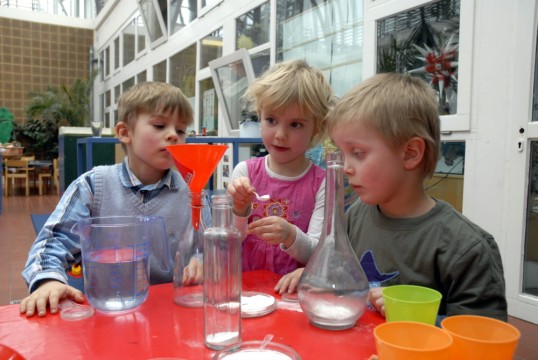 Kinder vor Versuchsanordnung mit Flaschen und Trichter