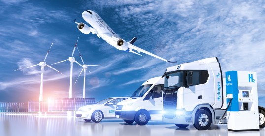 Bild auf dem mehrere Windkraftanlagen, Solarpanels, ein Flugzeug, LKWs und Zapfsäulen mit einem Hydrogen-Logo zu sehen sind.