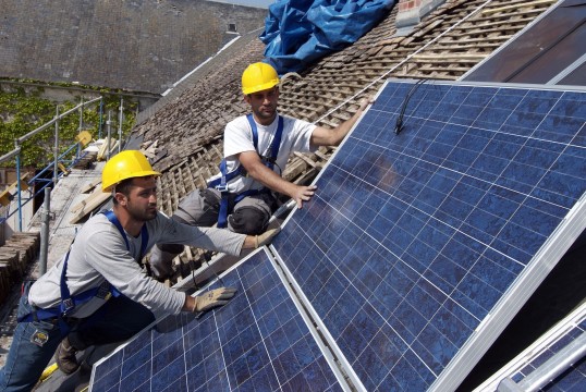 Photo:Two roofers mounting solar panels on an old roof. 
