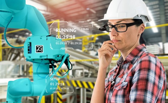 Photomontage: Woman with construction helmet and smart glasses looks at industrial robot, context information from the data glasses is superimposed