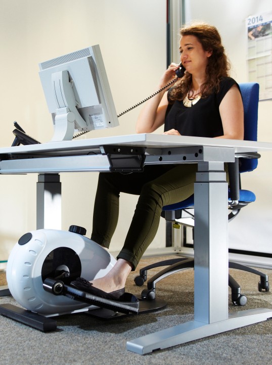 Woman at dynamic workplace with ergometer