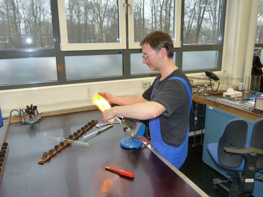 Foto: Mann in einer Werkstatt hält ein Werkstück in eine hell leuchtende Gasflamme