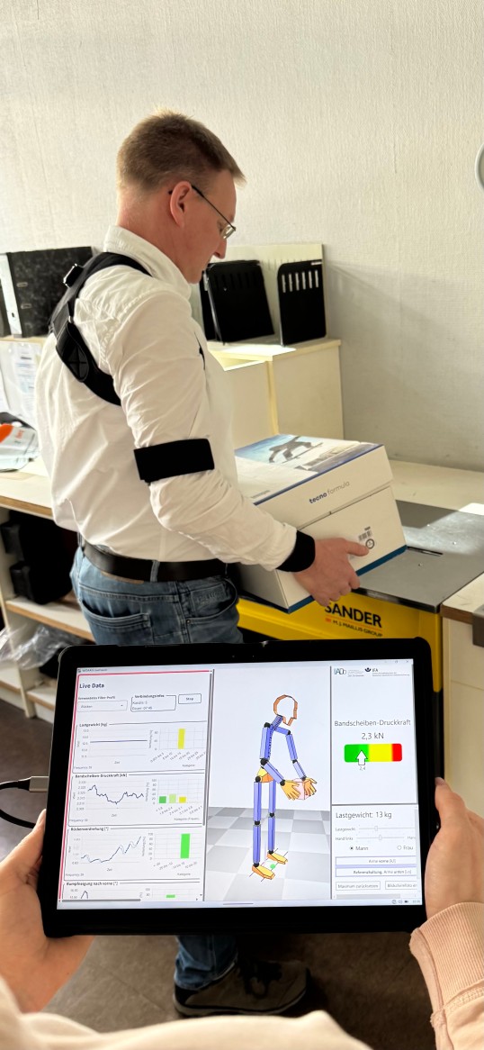 Foto: EIn Mann hebt einen Karton hoch, paralel ist das in einem 3D-Modell auf einem Tablett in der App zu sehen