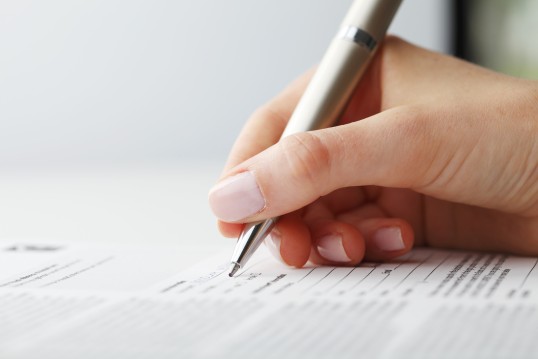 Foto: Eine weibliche Hand hält einen Kugelschreiber über ein Formular
