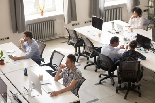 Foto eines Büros mit mehreren Arbeitsplätzen an denen Personen arbeiten.