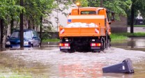 Foto: Bild einer Überschwemmungssituation mit einem Baufahrzeug und einem Schild.
