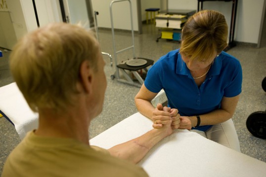 eine Therapeutin macht Bewegungsübungen der Hand mit einem Patienten