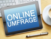 Bild eines Tablets, das auf einer Tastatur liegt, daneben steht eine Kaffeetasse, darunter liegt ein Stift. Auf dem Tablet steht in weißer Schrift auf blauem Hintergrund: Online-Umfrage.