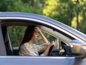 Eine junge Frau sitzt im Auto, sie wirkt erschöpft und greift an die Stirn.