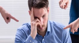 Eine männliche Person mit gesenktem Kopf wird von anderen Personen mit dem Zeigefinger schikaniert.