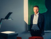Person steht vor einem Overhead-Projektor und schaut in die Kamera.