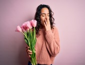 Bild einer Frau, die einen Blumenstrauß jält und sich die Nase zu hält.