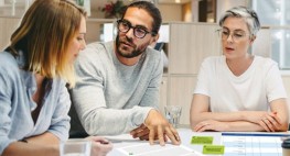 Bild von drei Personen am Tisch, vor ihnen liegt ein großes weißes Blatt Papier, darauf kleben rote und grüne Klebezettel.