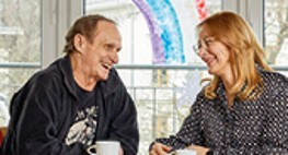 Bild von zwei Personen, die nebeneinander an einem Tisch sitzen und ein Gespräch führen.