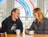 Bild von zwei Personen, die nebeneinander an einem Tisch sitzen und ein Gespräch führen.