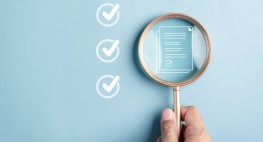 Eine Lupe schaut auf eine Checkliste, links davon sind Checkboxen mit weißen Haken.