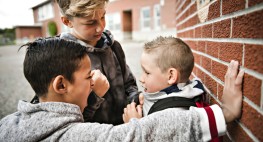 Foto: zwei Jungen bedrängen einen anderen auf dem Schulhof (die Szene ist gestellt)
