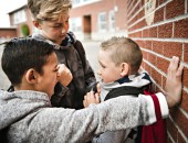 Foto: zwei Jungen bedrängen einen anderen auf dem Schulhof (die Szene ist gestellt)