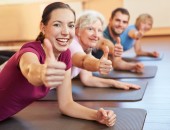 Auf Yogamatten sind fröhliche Personen verschiedener Alters zu sehen.
