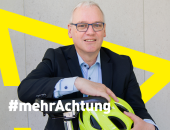 Bild von Dr. Stefan Hussy, der einen Fahrradhelm festhält, darauf in weißer Schrift der Hashtag: mehrAchtung!