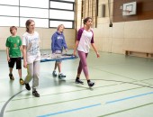 Kinder in der Sporthalle tragen ein Sportgerät.