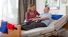 Bild von einer Person in einem Pflegebett, daneben steht eine Person, die sie pflegt.