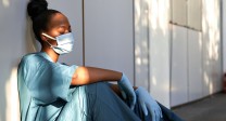 Foto: erschöpfte Krankenschwester mit Mundschutz, sitzt an Mauer gelehnt