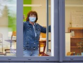 Foto: Eine Frau mit medizinischer Maske öffnet ein Fenster