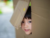 Foto: ein Kind schaut aus einer Pappkarton-Öffnung