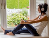 Foto: eine Frau sitzt mit geschlossenen Augen und Kopfhörer auf einem Fensterbrett 