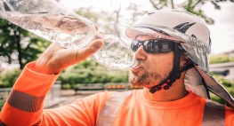 Foto: ein Bauarbeiter mit Helm, Nackenschutz und Sonnenbrille trinkt aus einer Wasserflasche