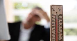 Bild eines Thermometers mit hohen Temperaturen, im Hintergrund unscharf ein Mann, der sich die Hand am Kopf hält 