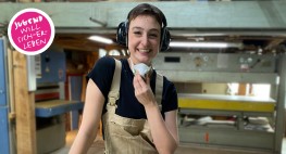 Foto: eine Frau steht in einer Werkstatt; sie hat Ohrschützer an und nimmt eine Atemschutzmaske ab.