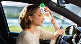 Foto: Eine Frau sitzt am Steuer eines Autos und kühlt ihre Stirn mit einer Flasche Wasser