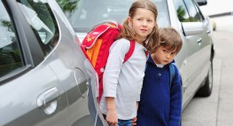 Bild von zwei Kindern, die zwischen zwei Autos hervorschauen und die Straße überqueren wollen.