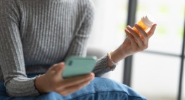 Foto: Eine Person mit Handy in einer Hand und Tabletten in der anderen Hand