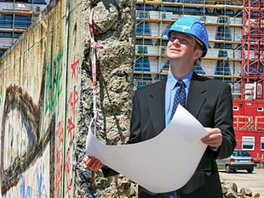 Bau-Ingenieur steht mit Bauplan vor einer Baustelle