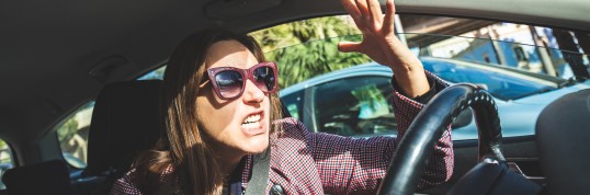 Eine Frau mit Sonnenbrille am Autolenkgrad, die sich aufgeregt 